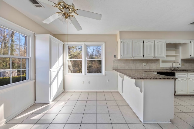 kitchen featuring kitchen peninsula, backsplash, sink, dark stone countertops, and white cabinetry