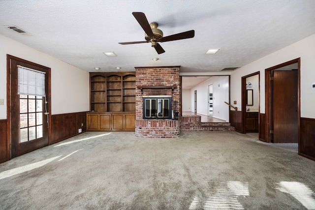 unfurnished living room featuring ceiling fan, wood walls, a textured ceiling, and a brick fireplace