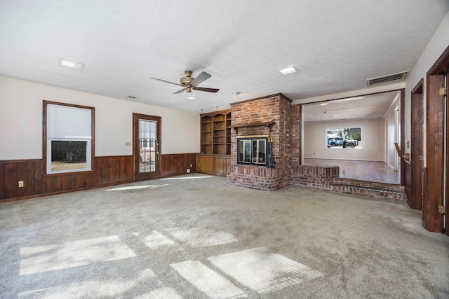 unfurnished living room with carpet flooring, ceiling fan, built in features, a fireplace, and a textured ceiling