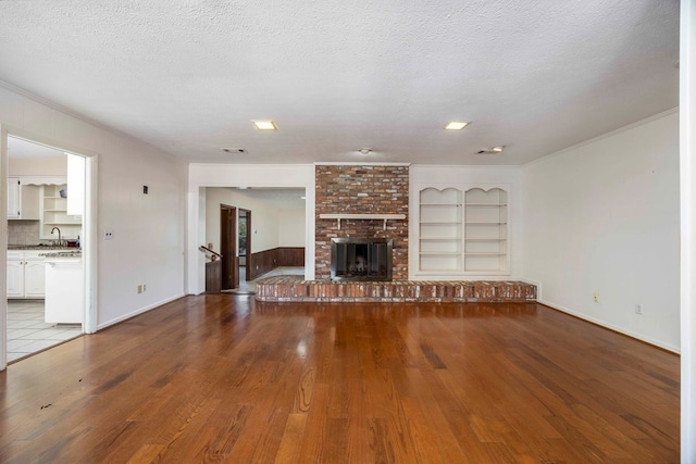 unfurnished living room featuring a fireplace, light wood-type flooring, built in features, and a textured ceiling