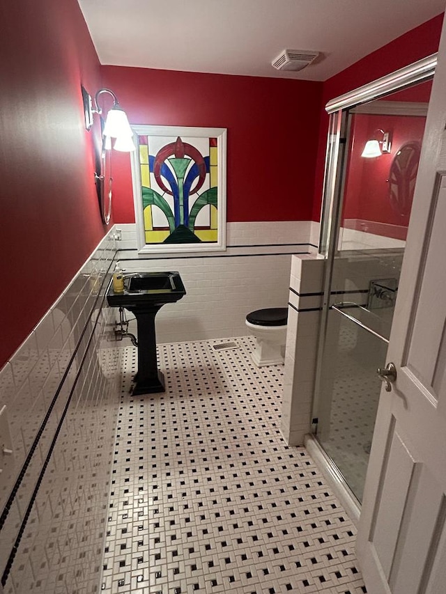 bathroom with sink, toilet, an enclosed shower, and tile walls