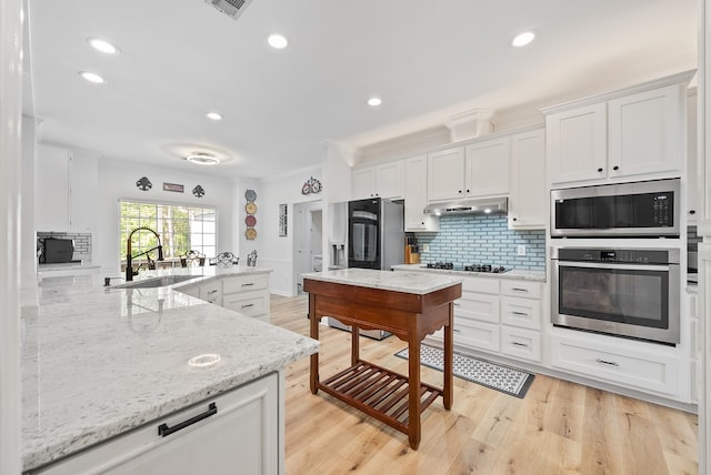 kitchen featuring decorative backsplash, white cabinetry, under cabinet range hood, a sink, and stainless steel appliances