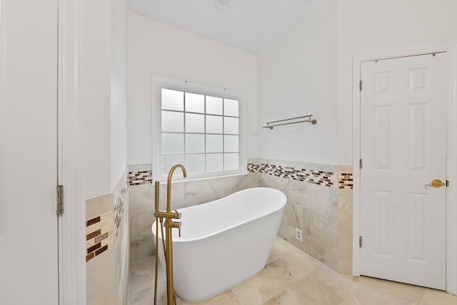 full bath featuring marble finish floor, a wainscoted wall, a soaking tub, and tile walls