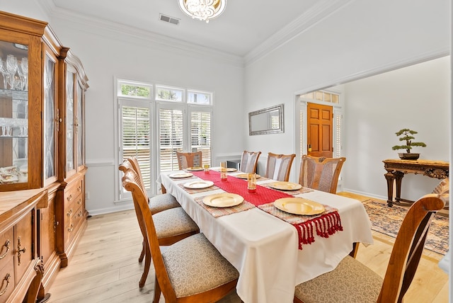 dining room featuring crown molding, visible vents, light wood-style flooring, and a wainscoted wall