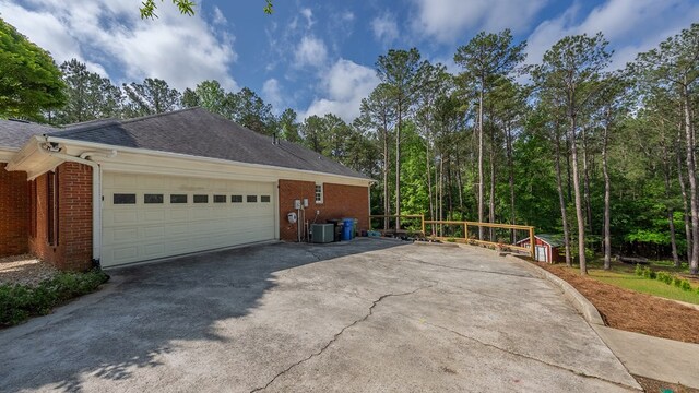 view of home's exterior with central AC unit, a shingled roof, driveway, and brick siding