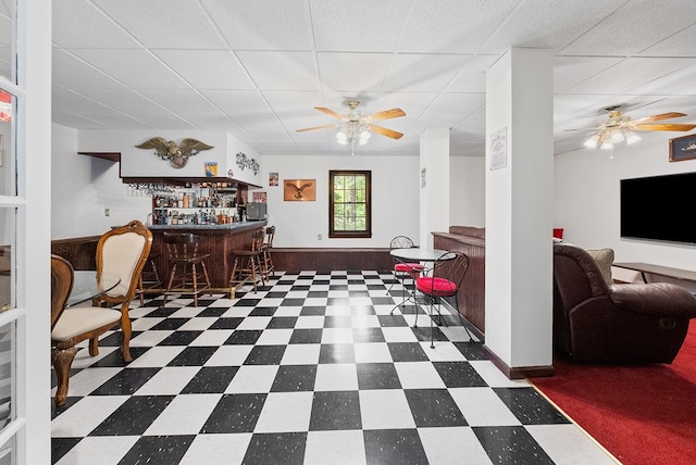 interior space with ceiling fan, a drop ceiling, a bar, and tile patterned floors