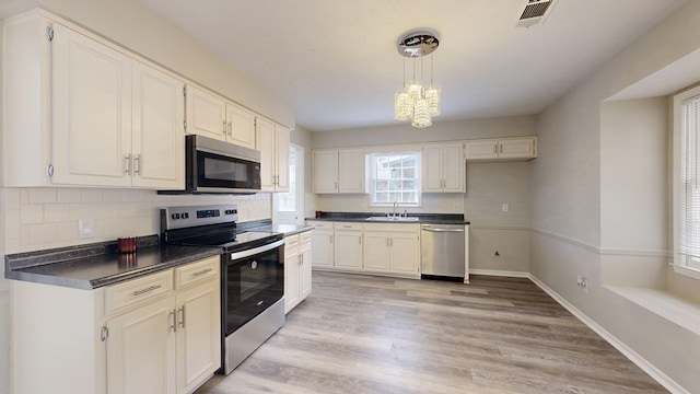 kitchen featuring appliances with stainless steel finishes, sink, white cabinets, and decorative light fixtures