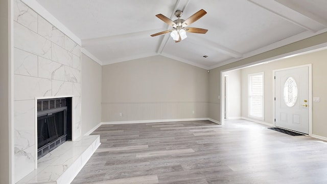 unfurnished living room featuring ceiling fan, a high end fireplace, light hardwood / wood-style flooring, and vaulted ceiling with beams