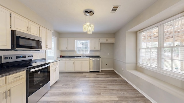 kitchen featuring sink, hanging light fixtures, stainless steel appliances, light hardwood / wood-style floors, and decorative backsplash