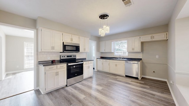 kitchen with pendant lighting, sink, light hardwood / wood-style flooring, appliances with stainless steel finishes, and white cabinetry