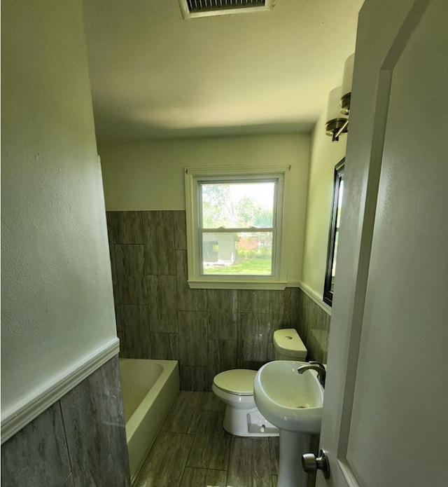 bathroom with tile walls, sink, toilet, and a bathing tub