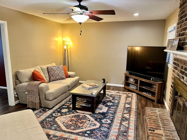 living area with a brick fireplace, baseboards, a ceiling fan, and wood finished floors