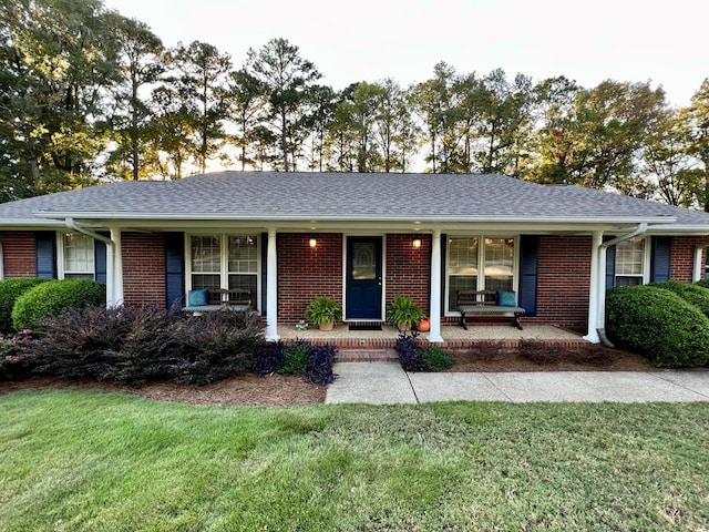 ranch-style home featuring brick siding, a porch, a front lawn, and roof with shingles