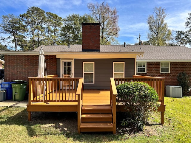 back of house with a wooden deck, a shingled roof, a chimney, a lawn, and brick siding