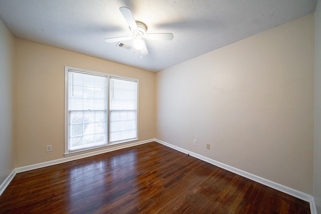 spare room with dark wood finished floors, a ceiling fan, visible vents, and baseboards