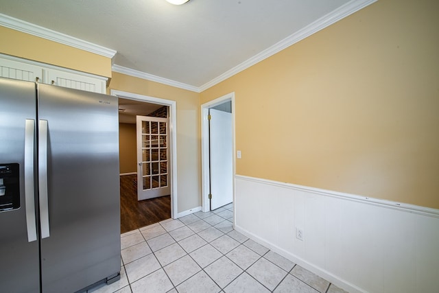 kitchen with a wainscoted wall, light tile patterned flooring, stainless steel fridge with ice dispenser, and ornamental molding