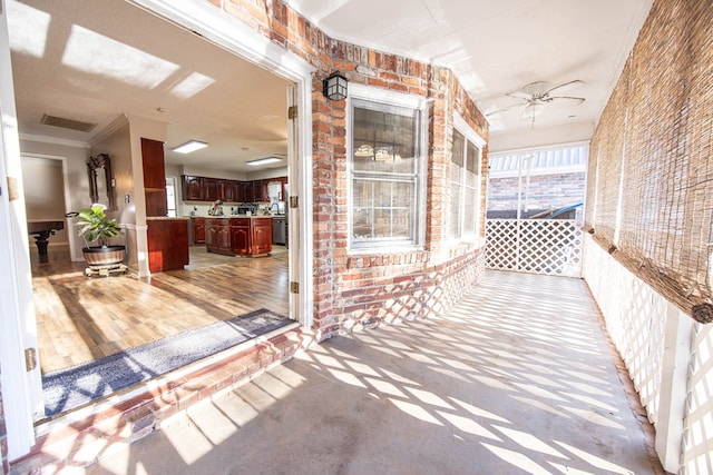 corridor with light wood-style flooring, brick wall, a sunroom, visible vents, and crown molding