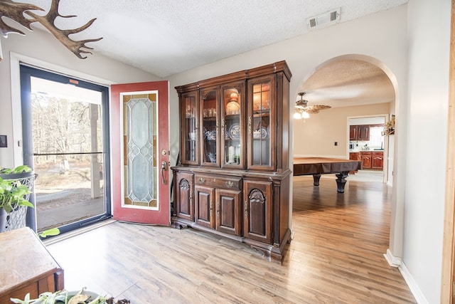 entrance foyer featuring light wood-style floors, arched walkways, visible vents, and a textured ceiling