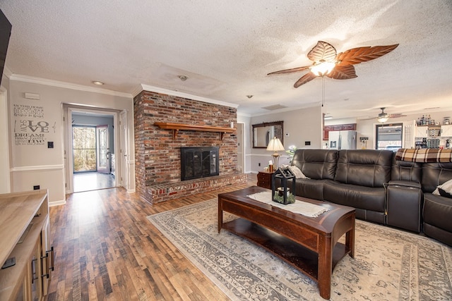 living area featuring a textured ceiling, baseboards, a brick fireplace, hardwood / wood-style floors, and crown molding