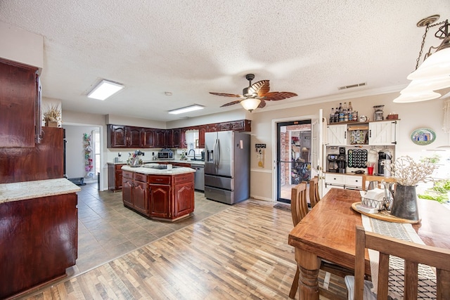 kitchen with visible vents, a kitchen island, appliances with stainless steel finishes, light countertops, and a sink