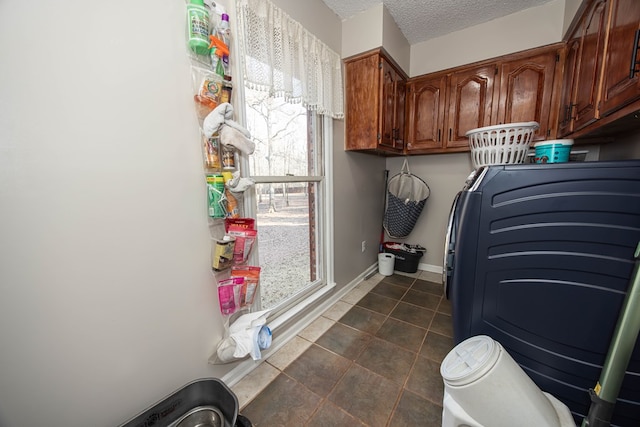 laundry area with cabinet space, washer / dryer, baseboards, a textured ceiling, and dark tile patterned floors