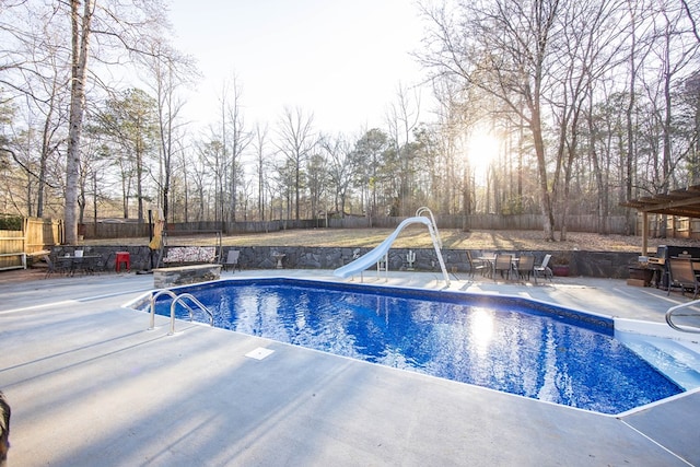 view of swimming pool with a patio area, a fenced backyard, a water slide, and outdoor dining space