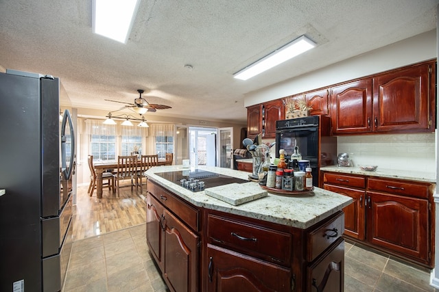 kitchen with decorative backsplash, a ceiling fan, a kitchen island, light stone countertops, and black appliances