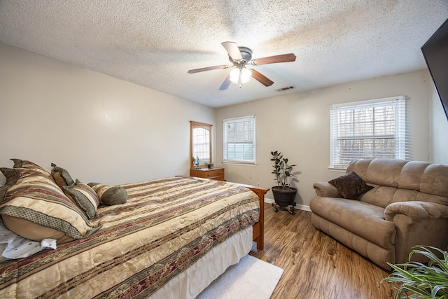 bedroom featuring ceiling fan, a textured ceiling, wood finished floors, visible vents, and baseboards