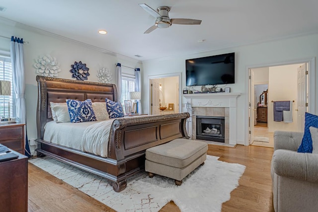 bedroom with ceiling fan, light wood-type flooring, a tile fireplace, and multiple windows