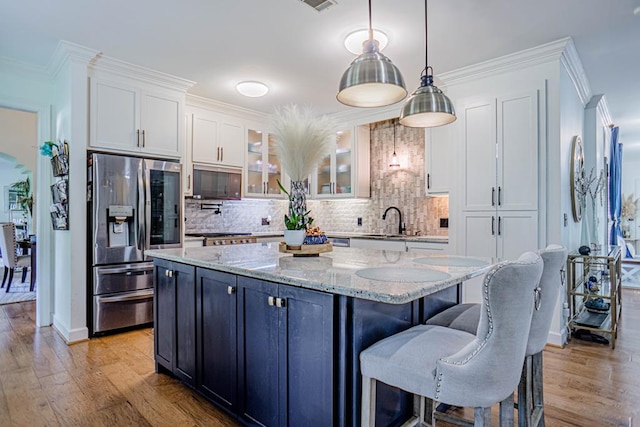 kitchen with stainless steel refrigerator with ice dispenser, white cabinets, light hardwood / wood-style floors, a kitchen island, and hanging light fixtures