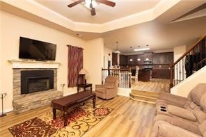 living room with hardwood / wood-style floors, ceiling fan, a fireplace, and a tray ceiling