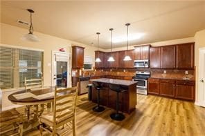 kitchen featuring a kitchen bar, light wood-type flooring, stainless steel appliances, pendant lighting, and a kitchen island