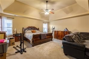 bedroom with light carpet, a raised ceiling, multiple windows, and ceiling fan