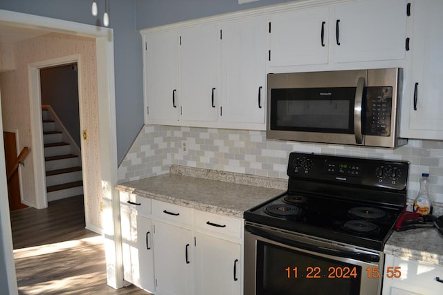 kitchen with electric range, white cabinetry, wood-type flooring, and backsplash