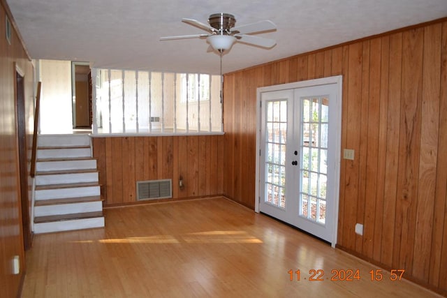 doorway with ceiling fan, light hardwood / wood-style floors, wooden walls, and french doors