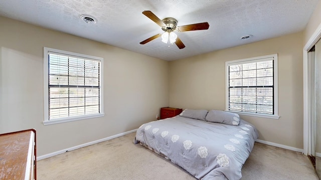 carpeted bedroom with ceiling fan, baseboards, visible vents, and a textured ceiling