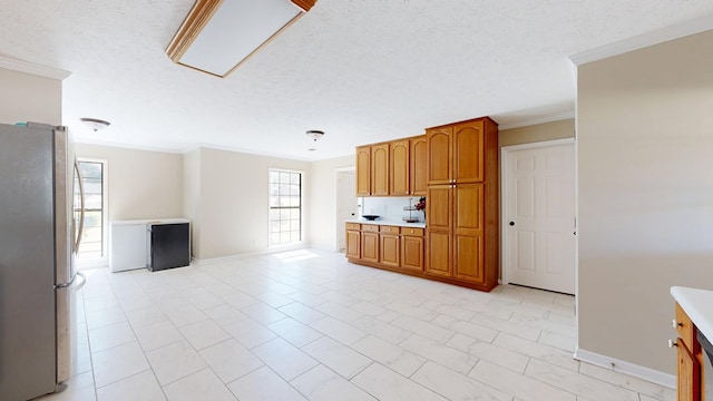 kitchen featuring brown cabinets, light countertops, freestanding refrigerator, and ornamental molding