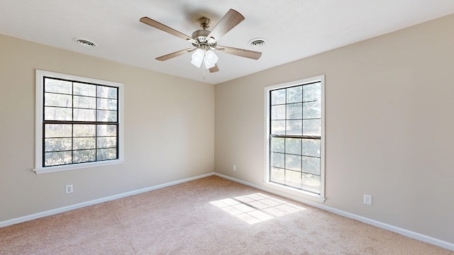 empty room with carpet, a ceiling fan, visible vents, and baseboards