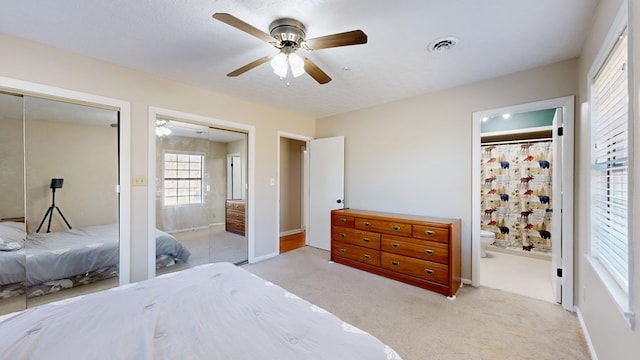 bedroom with a ceiling fan, visible vents, ensuite bath, multiple closets, and light colored carpet