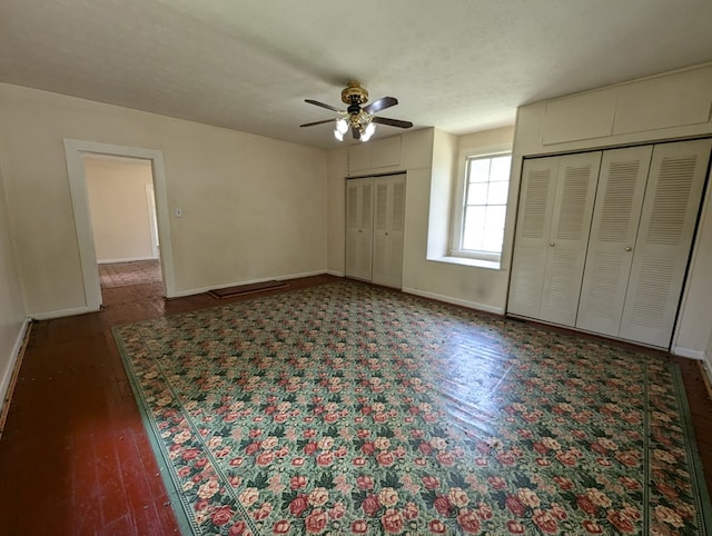 unfurnished bedroom with dark hardwood / wood-style flooring, a textured ceiling, two closets, and ceiling fan