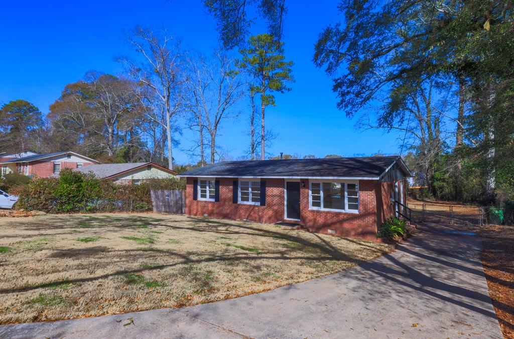 ranch-style house with driveway, fence, a front lawn, and brick siding