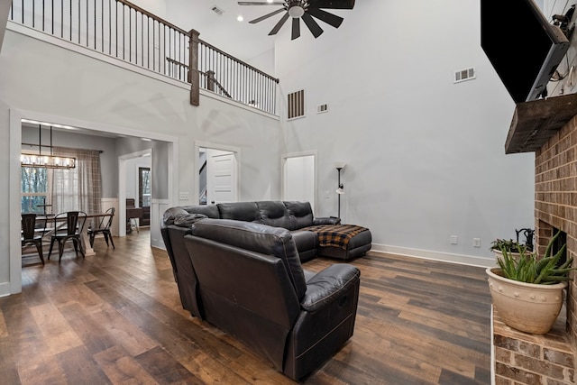 living room featuring dark wood-type flooring, ceiling fan with notable chandelier, and a brick fireplace