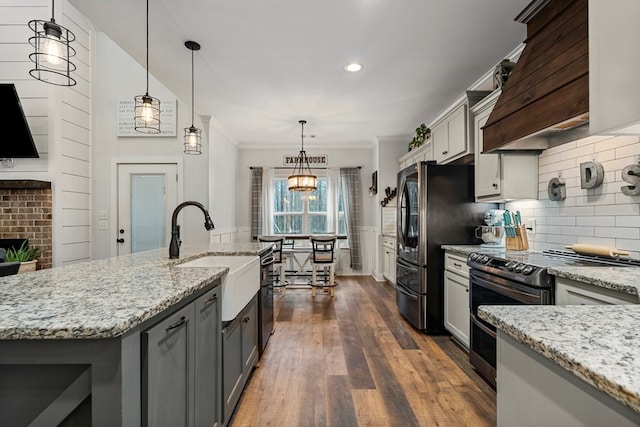 kitchen with sink, stainless steel range with electric cooktop, hanging light fixtures, an island with sink, and backsplash