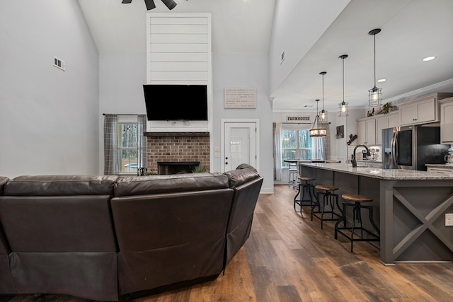 living room featuring sink, dark wood-type flooring, ceiling fan, high vaulted ceiling, and a fireplace