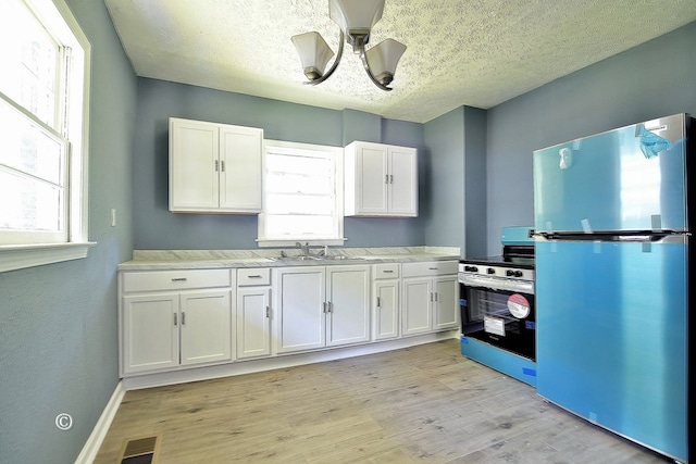 kitchen with white cabinetry, stainless steel fridge, plenty of natural light, and range