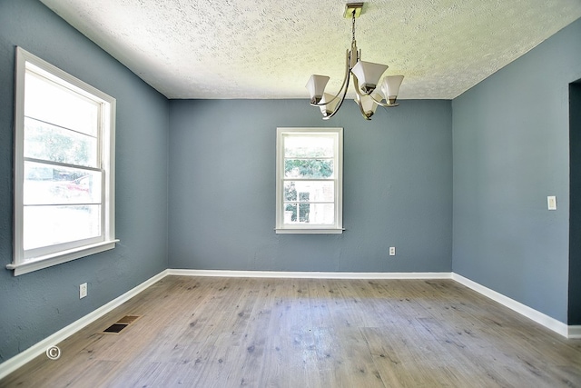 empty room with a textured ceiling, light hardwood / wood-style floors, and an inviting chandelier