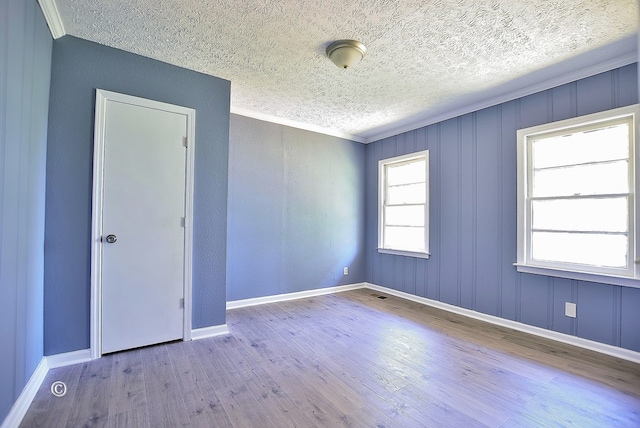 spare room featuring a wealth of natural light, ornamental molding, a textured ceiling, and light wood-type flooring