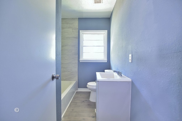 bathroom with a washtub, hardwood / wood-style floors, a textured ceiling, toilet, and vanity