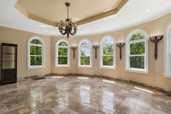 unfurnished sunroom with a raised ceiling, a wealth of natural light, and a chandelier