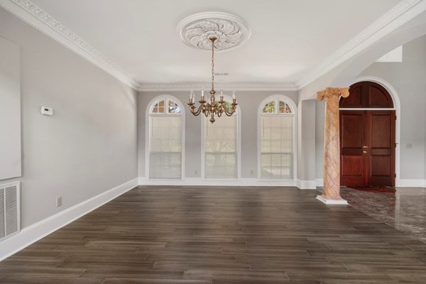 unfurnished dining area with dark hardwood / wood-style flooring, decorative columns, crown molding, and a notable chandelier